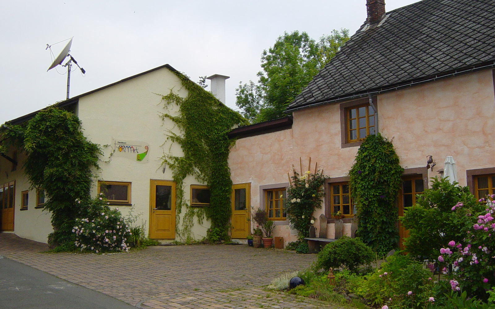 Außenansicht der Tischlerei FormArt mit Wohnhaus und efeubewachsener Schreinerei; im Vordergrund Blumen und Sträucher